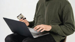 homem com laptop no colo e dinheiro na mão